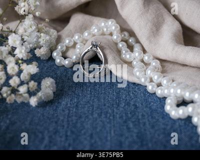 Rustic western wedding still life featuring engagement rings, pearl necklace, linen fabric and delicate white flowers arranged on blue denim Stock Photo