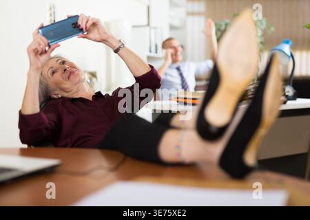 Mature woman office worker using smartphone during break Stock Photo