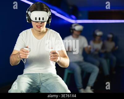 Guy playing game in virtual reality glasses in front of friends Stock Photo