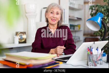 Smiling senior business woman working on laptop in office Stock Photo