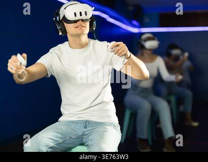 Guy playing game in virtual reality glasses in front of friends Stock Photo