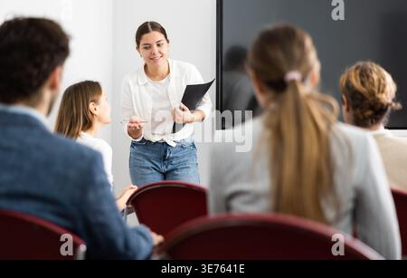 Positive skilled female coach explaining topic to group of people during foreign language class in auditory Stock Photo