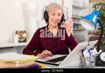Elderly businesswoman participating in web conference at workplace in office Stock Photo