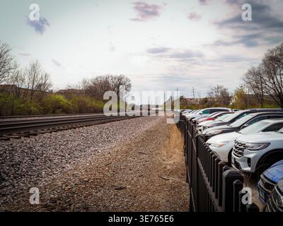 Railroad tracks running beside fenced parking lot with parked cars in suburban landscape under cloudy sky with leading lines perspective Stock Photo