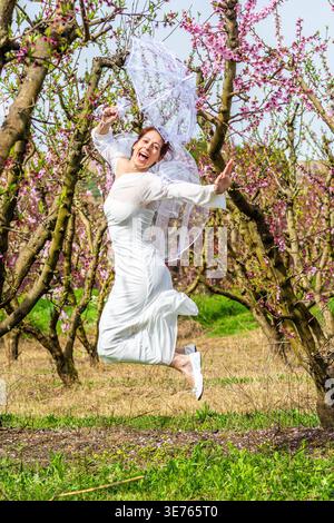 Bride joyfully jumping in blooming orchard during spring Stock Photo
