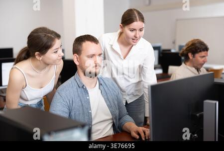 Two female friend companions stands next to computer courses male student Stock Photo