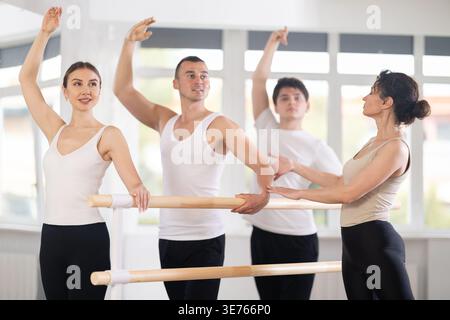 Group of ballet enthusiasts practicing at barre with experienced ballerina Stock Photo