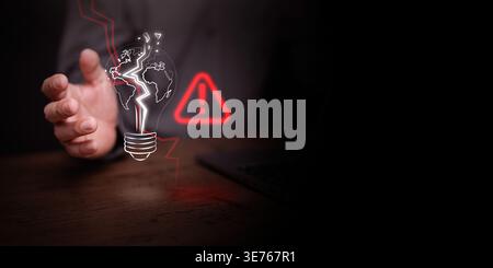cracked lightbulb globe and a red warning sign on a desk with a laptop. Concept of energy crisis and fragility, global power shortage, electricity mar Stock Photo
