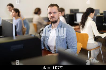 Guy student of computer courses looks at monitor screen, types on keyboard and does work Stock Photo
