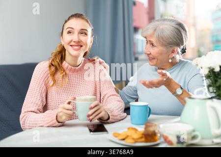 Senior mother and adult granddaughter having conversation and drinking tea Stock Photo
