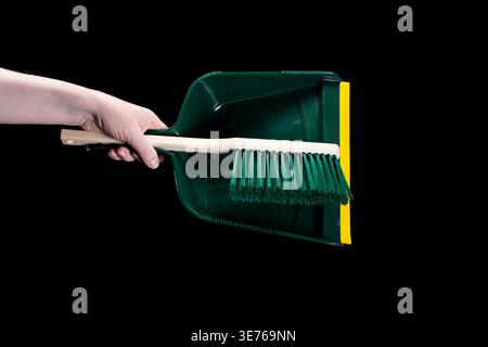 Hand holding green dustpan and brush on black background Stock Photo