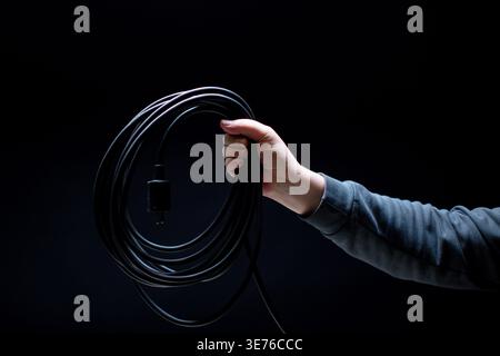 Hand holding black power cable on black background Stock Photo