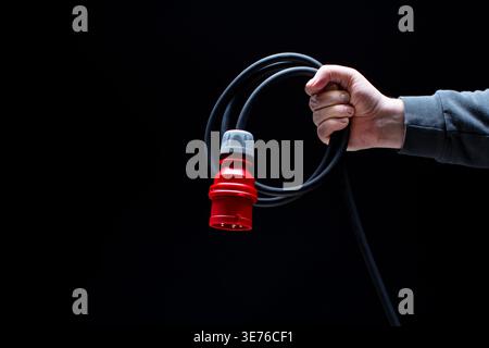 Hand holding red power connector on black background Stock Photo