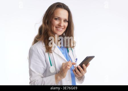 A friendly female doctor, in lab coat, smiles at camera while interacting with smartphone screen. This image depicts modern telemedicine for digital p Stock Photo