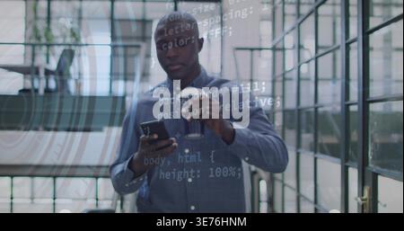 Holding phone, coffee cup, Black man in blue shirt checking code overlay on office glass partitions Stock Photo