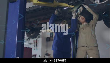 Inspecting mechanics wearing blue-beige coveralls under car on lift at garage with wrench and light Stock Photo
