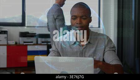 Working Black man in light gray shirt typing on silver laptop in office, with holographic globe Stock Photo
