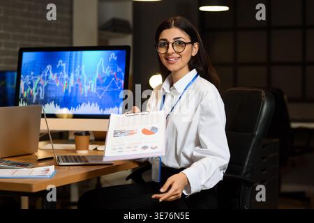 Female business analyst with diagrams in office at night. Data science concept Stock Photo