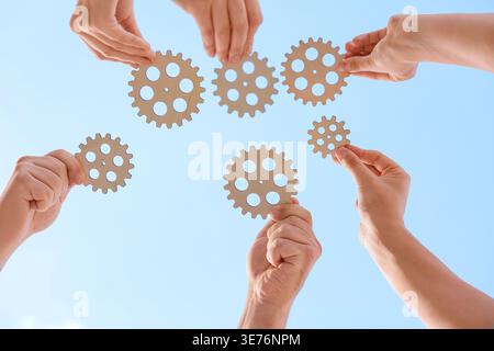 Many hands with wooden gears against sky, bottom view Stock Photo