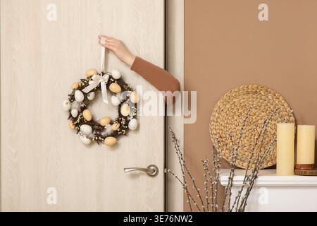 Female hand hanging Easter wreath on door in living room Stock Photo