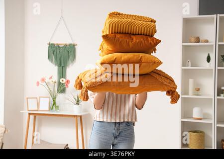 Woman holding stack of pillows with folded warm plaid in room Stock Photo