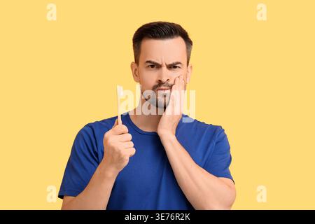 Handsome man with brush having toothache on yellow background Stock Photo