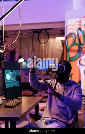 Hacker wearing vr helmet doing illegal activities and breaching online security systems in metaverse. African american man using virtual reality headset while cracking password Stock Photo