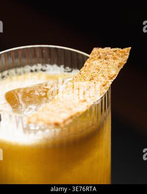 Golden drink with ice and crisp garnish. Crisp edge rests atop frothy surface. Warm glow highlights textured glass. Ideal for cocktail menus or bar sc Stock Photo