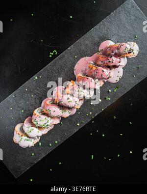 Delicate pink squid rings spiral elegantly on dark slate. Garnished with fresh green herbs and subtle seasoning. Perfectly plated, showcasing gourmet Stock Photo