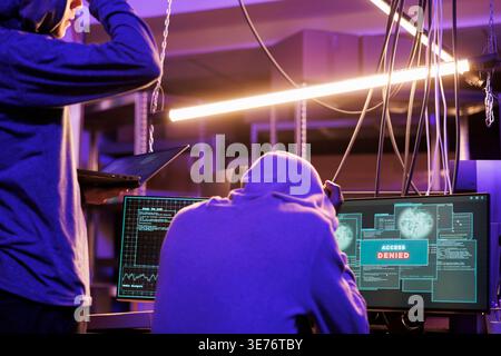 Upset hackers getting access denied message while hacking network system. Unhappy criminals breaking online server unsuccessfully on computer in abandoned warehouse at night Stock Photo