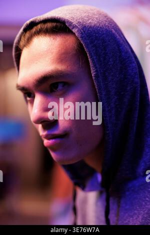 Smiling asian hacker in hood breaking into server and hacking database. Young man with smirk coding malicious ransomware and doing phishing criminal activity in hideout close up Stock Photo