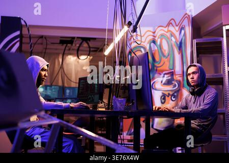 Hackers breaking law while coding dangerous computer virus in abandoned warehouse. Criminals working together and programming illegal malicious software in hideout workspace Stock Photo