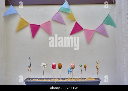 Easter decoration in flower box on house wall, colorful spring decoration with pennants and attached eggs, colorful Easter eggs as decoration, in fron Stock Photo