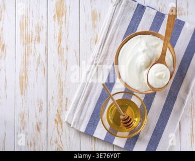 Tasty yogurt in wooden dish and jar of sweet honey on wooden table, top view Health food from yoghurt concept Stock Photo