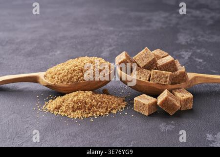 Brown sugar cubes and granulated sugar in two spoons with white sugar on black table.Top view .Raw organic cane sugar Stock Photo