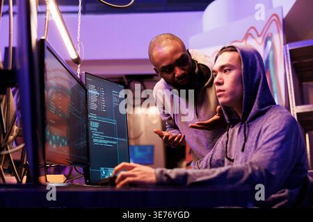 Hackers discussing cyberattack while checking spying online and using malware on computer. Asian and african american young criminals talking about password cracking methods Stock Photo