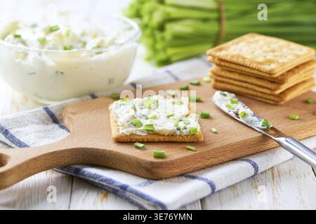 Crispy Crackers and a Glass Bowl with a Cream Cheese Spread and Cut Chives on a Light Kitchen Table Stock Photo