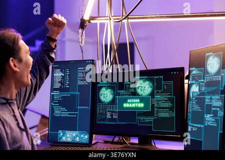 Hacker celebrating access granted to computer system and doing illegal activities. Young asian man raising fist in victory gesture after hacking database successfully in abandoned warehouse Stock Photo