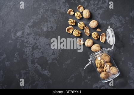 Peeled and unpeeled walnuts in an open glass container on a black table, with copy space. View from above Stock Photo