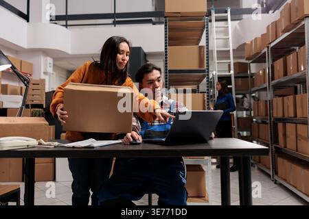 Shipment service workers managing parcel receiving and sending operations in post office storage room. Industrial warehouse asian workers team supervising goods inventory using computer software Stock Photo