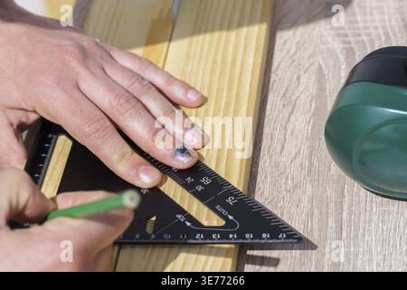 Person using a triangle square to draw a line on a wooden board with a pencil, showing an injured finger with a subungual hematoma, highlighting a com Stock Photo