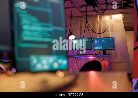 Computer screens with malware running code stealing sensitive information in hackers abandoned warehouse. Malicious software with internet virus on monitors in dark hideout with neon light Stock Photo