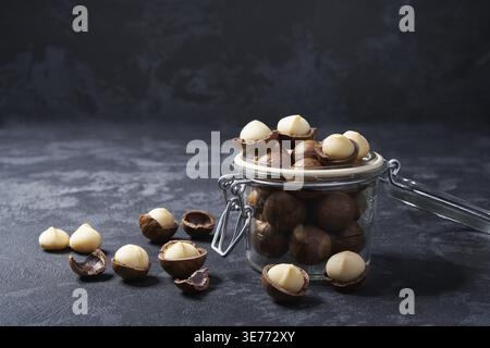 Macadamia nuts in an open glass jar on a black background, close-up view Stock Photo