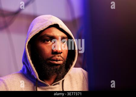 African american hacker breaching system security and stealing sensitive information. Young criminal in hood breaking law while cracking password and using spyware close up Stock Photo