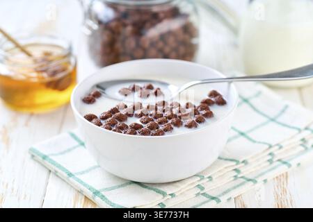 Bowl of tasty chocolate corn balls with milk and honey on a light kitchen table. healthy breakfast with cereal flakes. chocolate corn balls and milk, Stock Photo