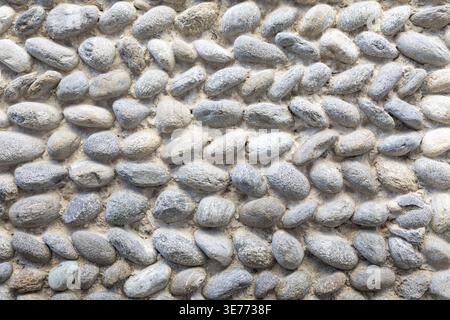 Close-up of a pebble stone wall surface made of smooth rounded rocks. Natural pattern and neutral tones create a calm, balanced, and timeless architec Stock Photo