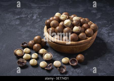 Organic macadamia nuts in a wooden bowl on a black background, close-up Stock Photo