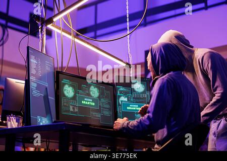 Hackers getting access granted while breaking into online server on computer. Two smiling criminals happy after successful ddos attack on website in abandoned warehouse at night Stock Photo