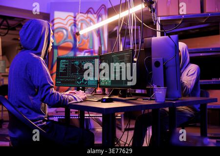 Hackers committing internet crime while breaking into server and stealing privacy information. Cybercriminals planning phishing and doing online scam on computer in dark room hideout Stock Photo