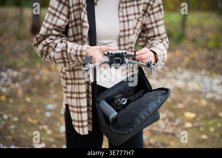 Woman unfolds drone and prepares it for flight. Close up of hands setting up quadcopter outdoors, adjusting arms and checking camera, concept of preparation, hobby and technology Stock Photo